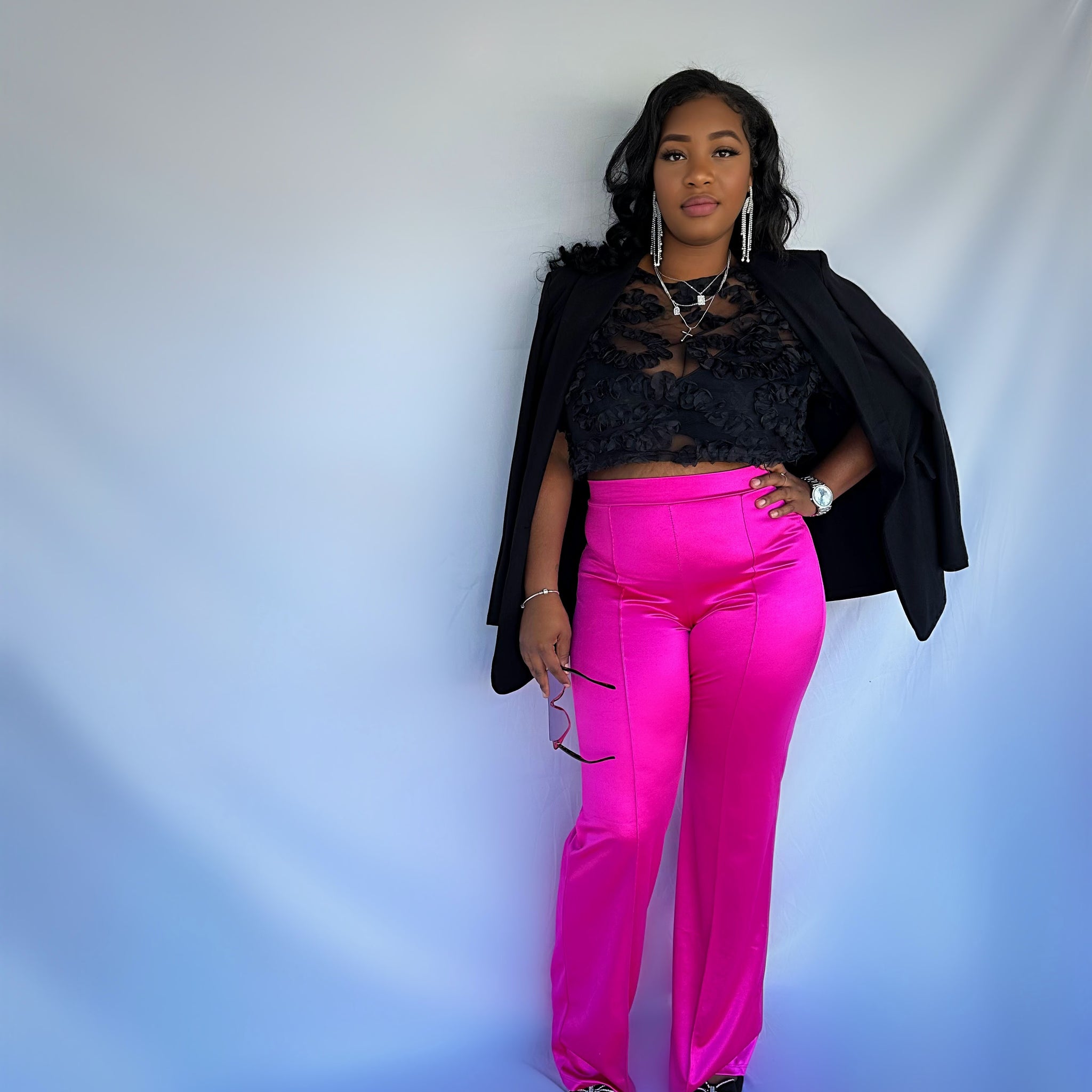 A model wearing bright pink high waisted pleated pants with a back zipper, paired with a black top and accessories.