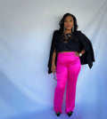 A model wearing bright pink high waisted pleated pants with a back zipper, paired with a black top and accessories.